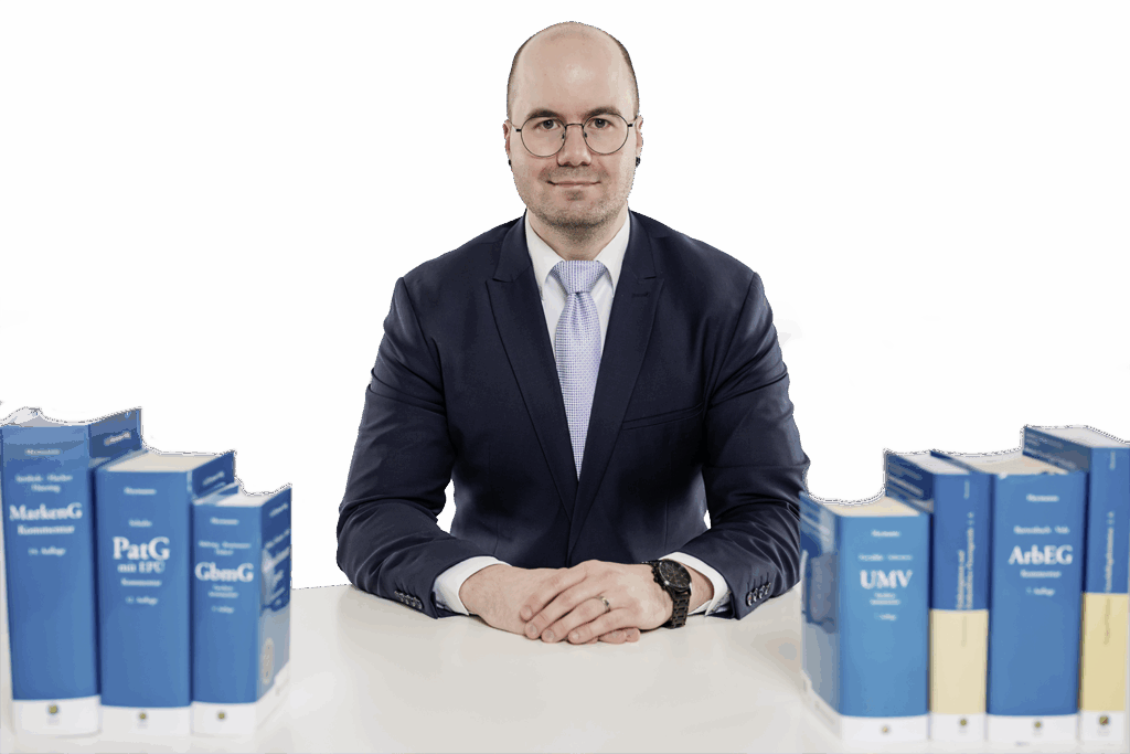 Patentanwalt Philipp Avon sitzt vertrauensvoll an einem Schreibtisch mit Fachbüchern
