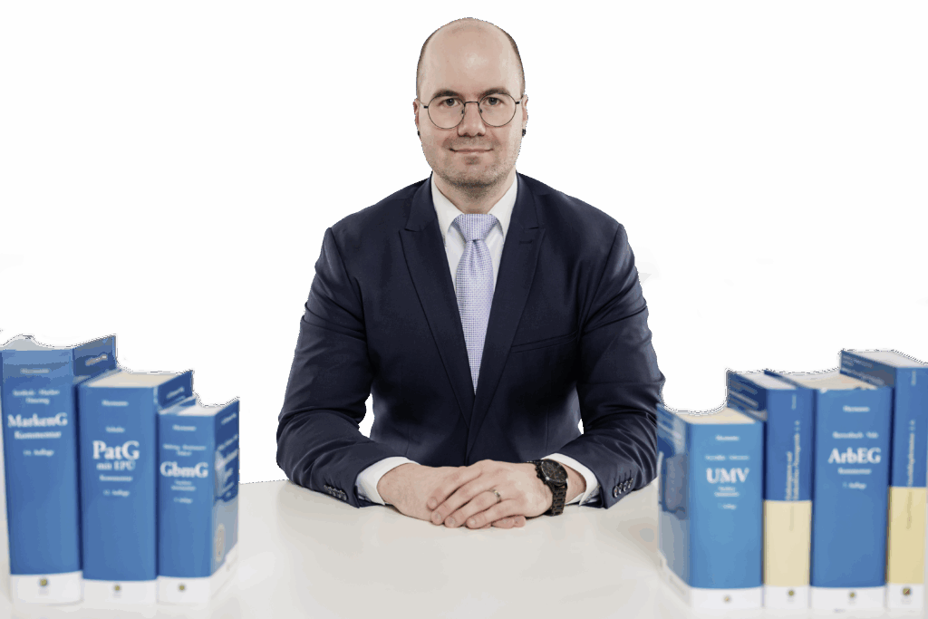 Patentanwalt Philipp Avon sitzt vertrauensvoll an einem Schreibtisch mit Fachbüchern
