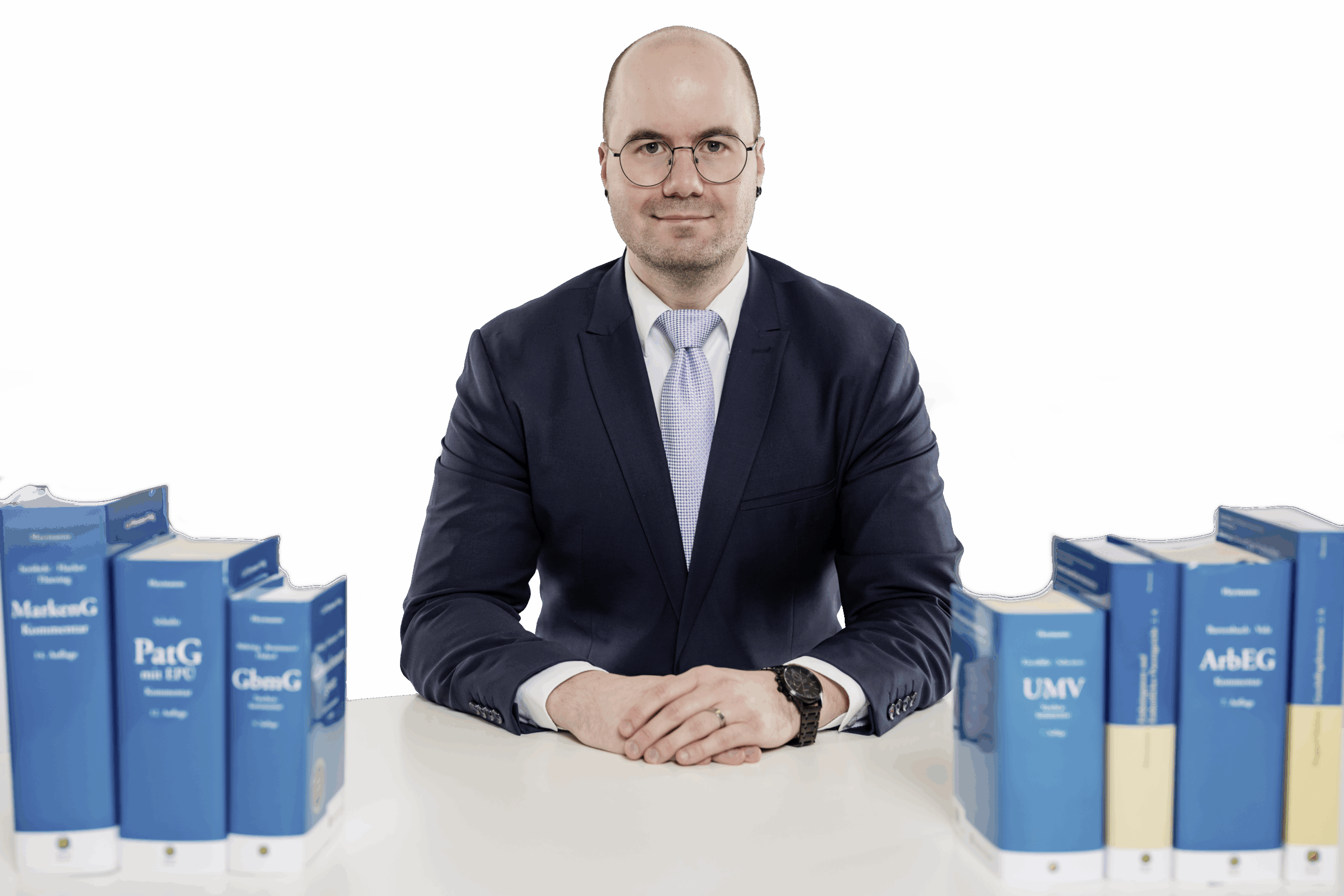 Patentanwalt Philipp Avon sitzt vertrauensvoll an einem Schreibtisch mit Fachbüchern