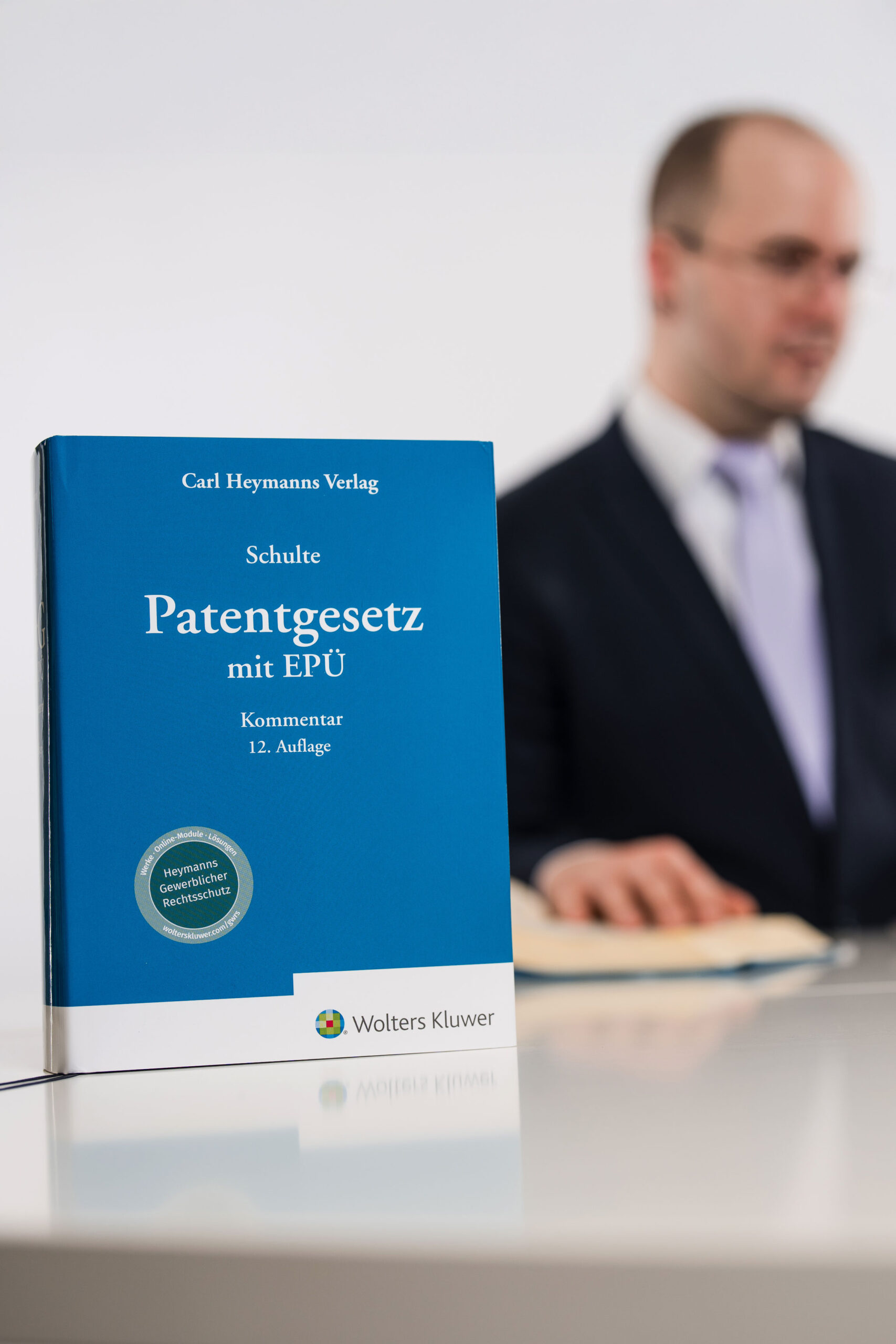 Patentanwalt Philipp Avon sitzt am Schreibtisch. Im Vordergrund steht das Buch über Patentschutz